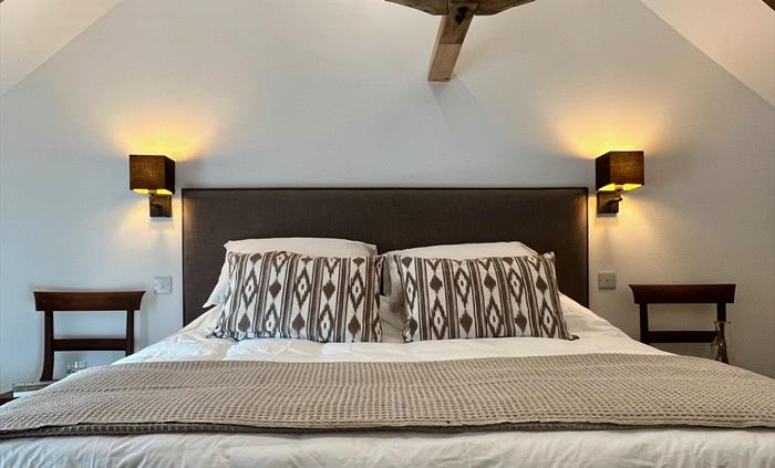 The main bedroom includes a king size bed with wall lights and chairs either side and original roof truss above.
